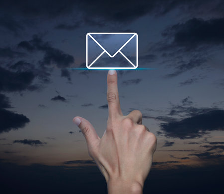 Hand pressing email flat icon over sunset sky, Business contact us online conceptの写真素材