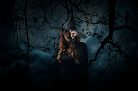 Scary halloween witch standing over dead tree, crow, birds, full moon and spooky cloudy sky, Halloween mystery conceptの写真素材