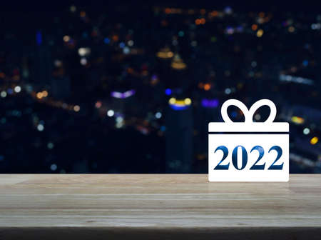 Gift box happy new year 2022 flat icon on wooden table over blur colorful night light modern city tower and skyscraper, Business shop online conceptの写真素材