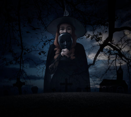Halloween witch holding black face mask standing over grass, dead tree, cross, birds with church and spooky cloudy sky, Halloween mystery conceptの写真素材
