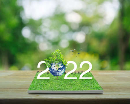 2022 white text with planet and tree on green grass on open book on wooden table over blur green tree in park, Happy new year 2022 ecological cover, Save the earth concept, Elements of this image furnished by NASAの写真素材