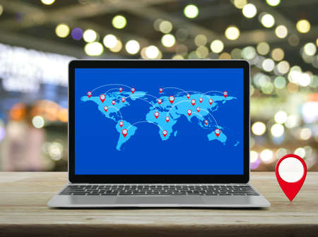 Map pin location button with connection line and world map on modern laptop computer on wooden table over blur of shopping mall, Map pointer navigation online concept, Elements of this image furnished by NASAの写真素材