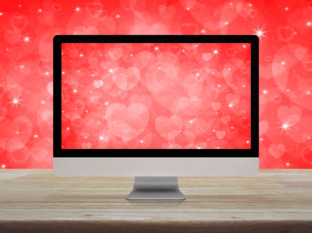Desktop modern computer monitor with love heart screen on wooden table over red background, Business...