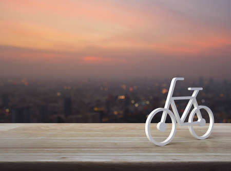 Bicycle 3d icon on wooden table over blur of cityscape on warm light sundown, Business bicycle service conceptの写真素材