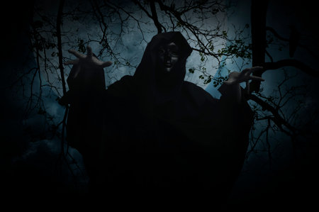 Grim reaper standing over dead tree, crow, birds, full moon and spooky cloudy sky, Halloween mystery conceptの写真素材