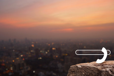 Phone icon with copy space for add your phone number on rock mountain over blur of cityscape on warm...
