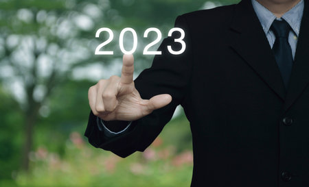Businessman pressing 2023 letter over blur flower and tree in park, Business happy new year 2023 cover conceptの写真素材