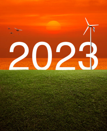 2023 white text with wind turbine on green grass field over sunset sky and sea with birds, Happy new...