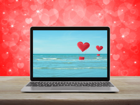 Red fabric heart love air balloon on tropical sea with modern laptop computer on wooden table over blur red wall, Business internet dating online, Valentines day conceptの写真素材