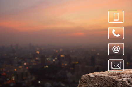Telephone, mobile phone, address and email icon on rock mountain over blur of cityscape on warm light sundown, Business customer service and support online conceptの写真素材