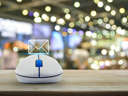 Mail flat icon with wireless computer mouse on wooden table over blur light and shadow of shopping mall, Business contact us online conceptの写真素材