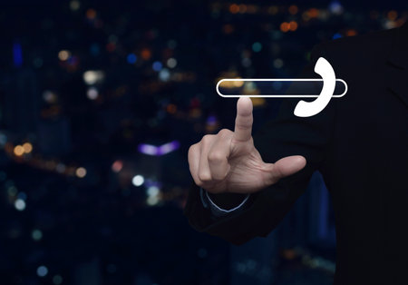 Businessman pressing phone icon with copy space for add your phone number over blur colorful night light city tower and skyscraper, Business contact us conceptの写真素材