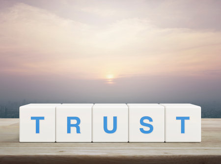 Trust letter on white block cubes on wooden table over modern city tower and skyscraper at sunset, vintage style, Building trust business conceptの写真素材