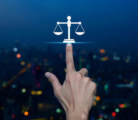 Hand pressing law flat icon over blur colorful night light modern city tower and skyscraper, Business legal service conceptの写真素材