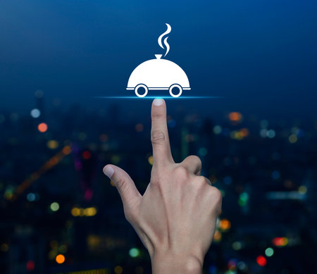 Hand pressing restaurant cloche flat icon over blur colorful night light modern city tower and skyscraper, Business food delivery online conceptの写真素材