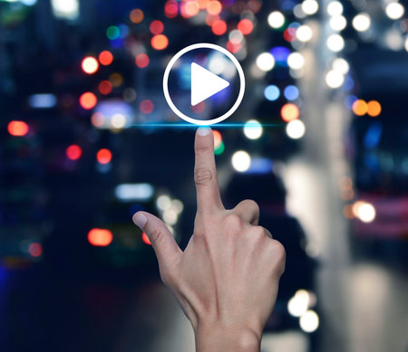 Hand pressing play button flat icon over blur colourful night traffic jam road in city, Business music online conceptの写真素材