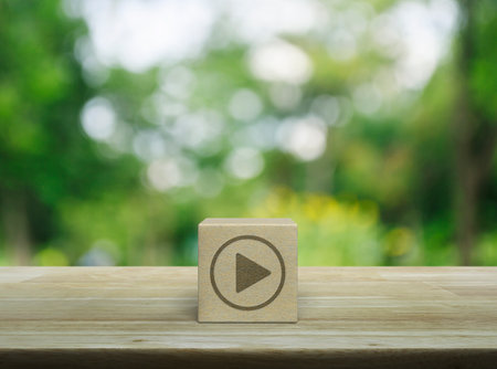 Play button icon on wood block cube on wooden table over blur green tree in park, Business music online conceptの写真素材