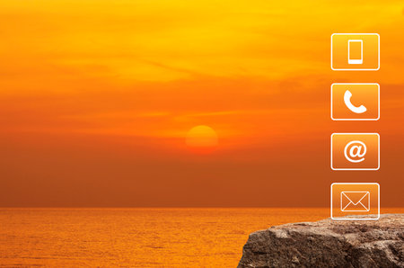 Telephone, mobile phone, address and email icon on rock mountain over sunset sky and sea, Business customer service and support online conceptの写真素材