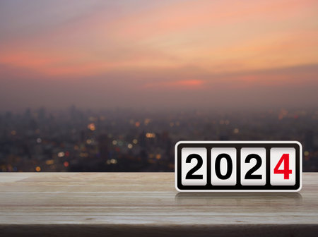 Retro flip clock with 2024 text on wooden table over blur of cityscape on warm light sundown, Happy new year 2024 cover conceptの写真素材