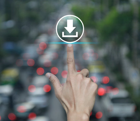 Hand pressing download flat icon over blur of rush hour with cars and road in city, Technology internet online conceptの写真素材