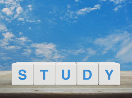 Study letter on white block cubes on wooden table over blue sky with white clouds, Business, education and learning conceptの写真素材