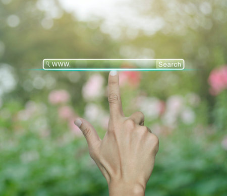 Hand pressing search www button over blur pink flower and tree in park, Searching system and internet conceptの写真素材