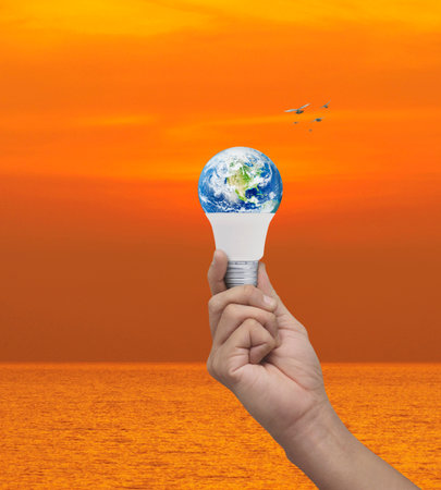 Hand holding earth globe inside led light bulb over sunset sky and sea, Green ecology and saving...