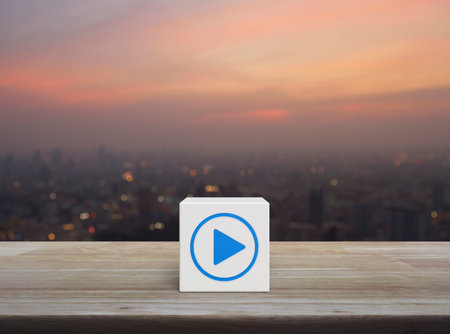Play button icon on white block cube on wooden table over blur of cityscape on warm light sundown, Business music online conceptの写真素材