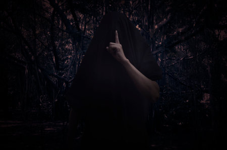 Grim reaper showing silence sign with finger standing over spooky dark forest with tree, leaves and vine, Halloween mystery conceptの写真素材