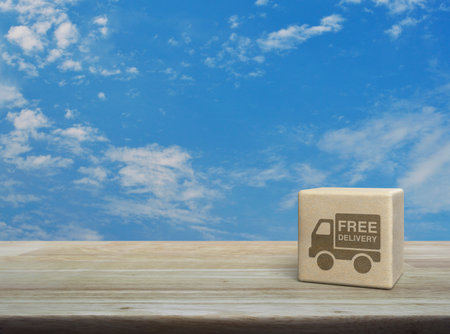 Free delivery truck icon on wood block cube on wooden table over blue sky with white clouds, Business transportation service conceptの写真素材