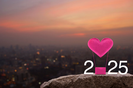 Pink fabric heart love air balloon with 2025 white text on rock mountain over cityscape on warm light sundown, Happy new year and Valentines day 2025 conceptの写真素材