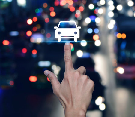 Hand pressing car flat icon over blur colourful night traffic jam road in city, Business transportation service conceptの写真素材