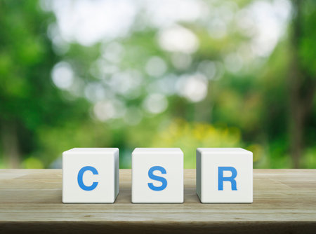 CSR acronym on white block cubes on wooden table over blur green tree in park, Corporate Social Responsibility conceptの写真素材