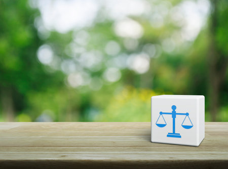 Law flat icon on white block cube on wooden table over blur green tree in park, Business legal service conceptの写真素材
