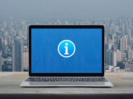 Information sign icon on modern laptop computer screen on wooden table over city tower and skyscraper, Business customer service and support online conceptの写真素材