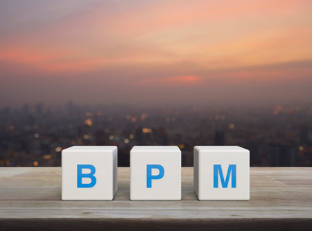 BPM acronym on white block cubes on wooden table over blur of cityscape on warm light sundown, Business process management conceptの写真素材