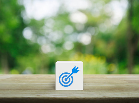 Target with dart flat icon on white block cube on wooden table over blur green tree in park, Business success conceptの写真素材