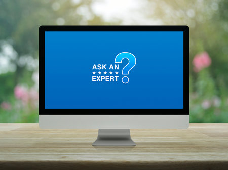 Ask an expert with star and question mark sign icon on desktop modern computer monitor screen on wooden table over blur park, Technology communication online conceptの写真素材