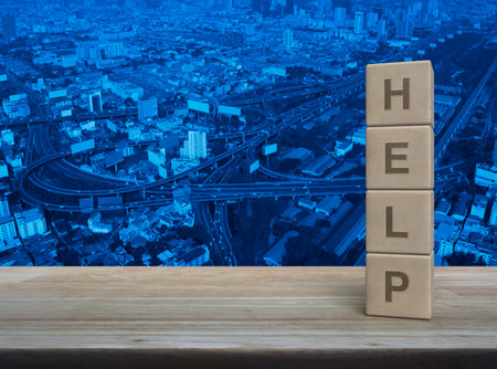 HELP letter on wood block cubes on wooden table over modern city tower, street, expressway and skyscraper, Business customer service and support conceptの写真素材