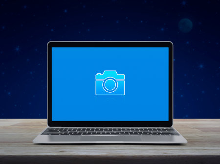 Camera flat icon on modern laptop computer screen on wooden table over fantasy night sky and moon, Business camera service shop online conceptの写真素材