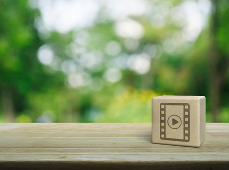 Play button with movie flat icon on wood block cube on wooden table over blur green tree in park, Business cinema online conceptの写真素材