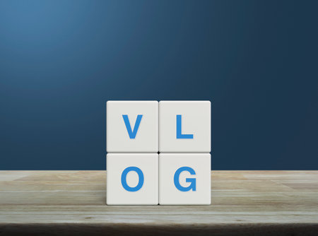 Vlog letter on white block cubes on wooden table over light blue wall, Vlog video marketing conceptの写真素材