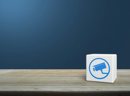 Cctv camera flat icon on white block cube on wooden table over light blue wall, Technology security and safety online conceptの写真素材