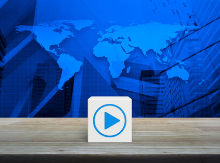 Play button icon on white block cube on wooden table over world map, modern office city tower and skyscraper, Business music online concept, Elements of this image furnished by NASAの写真素材