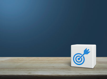 Target with dart flat icon on white block cube on wooden table over light blue wall, Business...