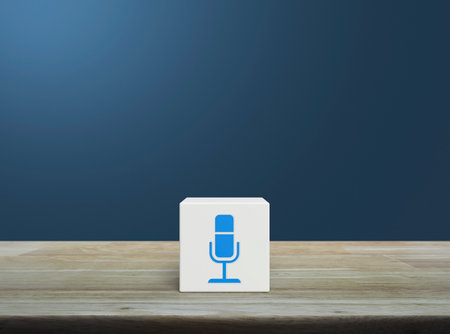 Microphone flat icon on white block cube on wooden table over light blue wall, Technology communication conceptの写真素材