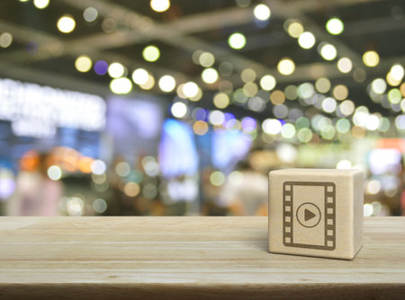 Play button with movie flat icon on wood block cube on wooden table over blur light and shadow of shopping mall, Business cinema online conceptの写真素材