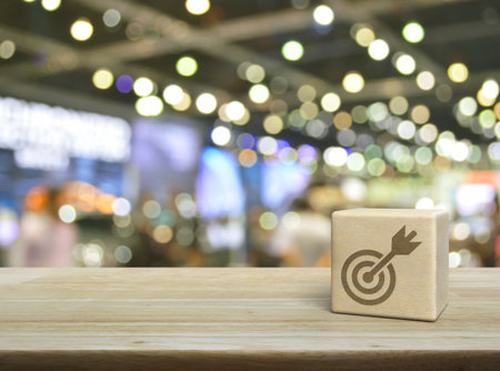 Target with dart flat icon on wood block cube on wooden table over blur light and shadow of shopping mall, Business success conceptの写真素材