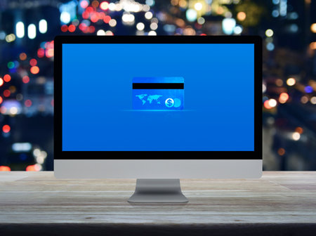 Credit card on modern computer monitor screen on wooden table over blur colorful night light traffic...