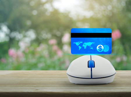 Credit card on wireless computer mouse on wooden table over blur pink flower and tree in park, Online e-payment concept, Elements of this image furnished by NASAの写真素材